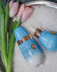 Two skincare products on a textured surface with tulips in the background