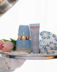 Two skincare products on a tray with tulips and a floral towel.