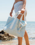 Person holding a light blueBloomeffects tote bag on a beach