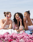 Three women sitting on pink flowers, smiling and using Bloomeffects products.