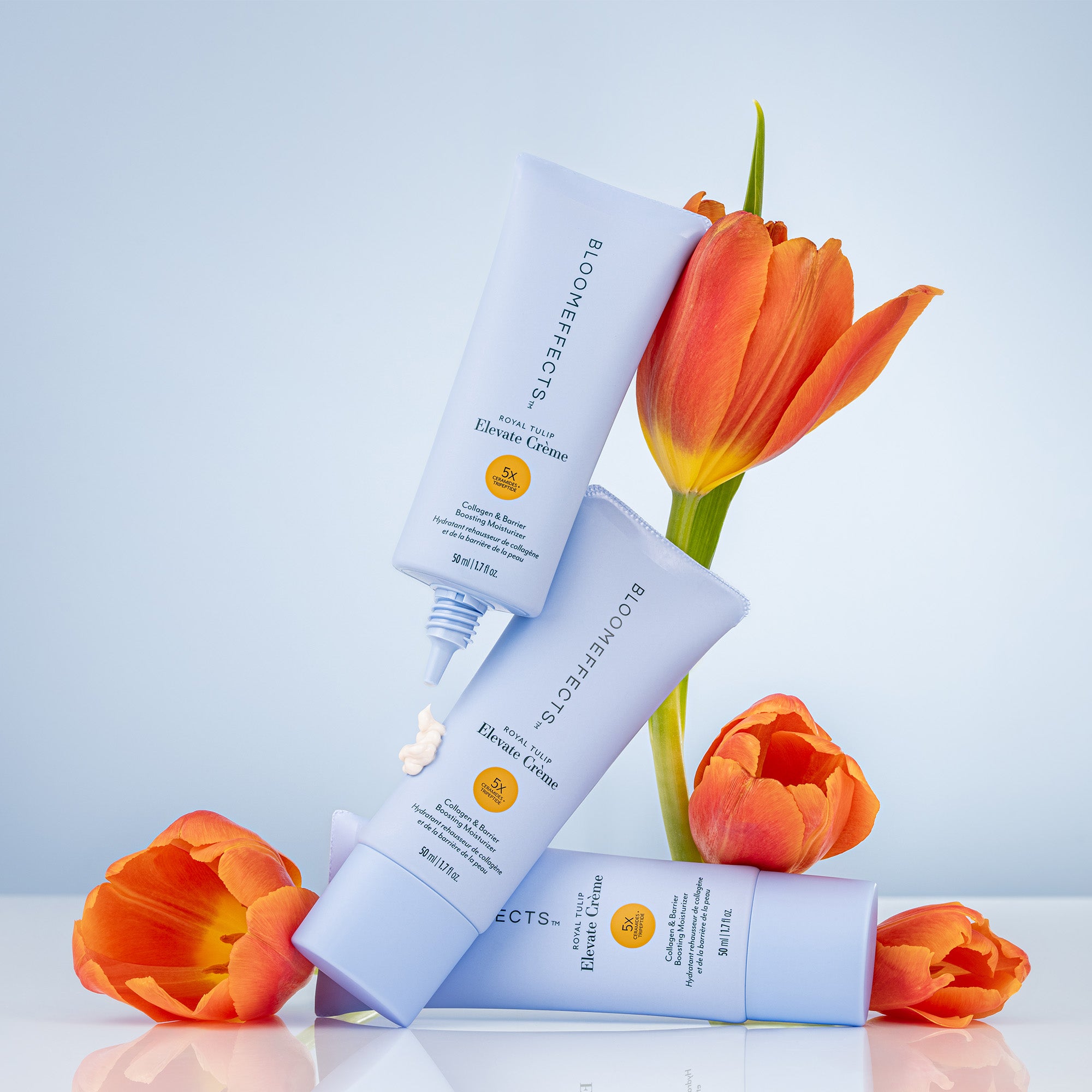 Three bottles of Bloomeffects Elevate with orange tulips on a light background
