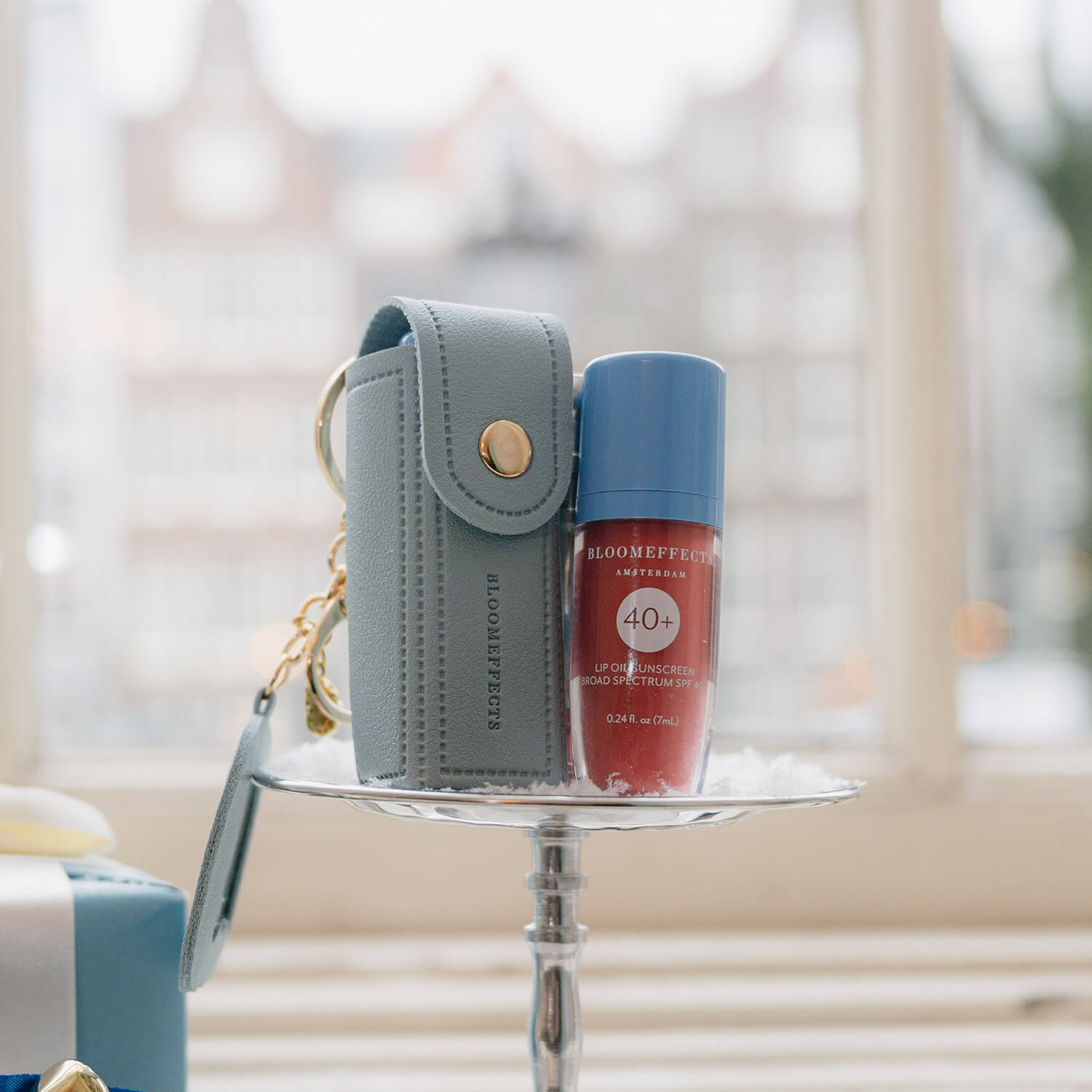 Small gray pouch with a keychain and a red bottle  of tulipscreen lip oil with a blurred background