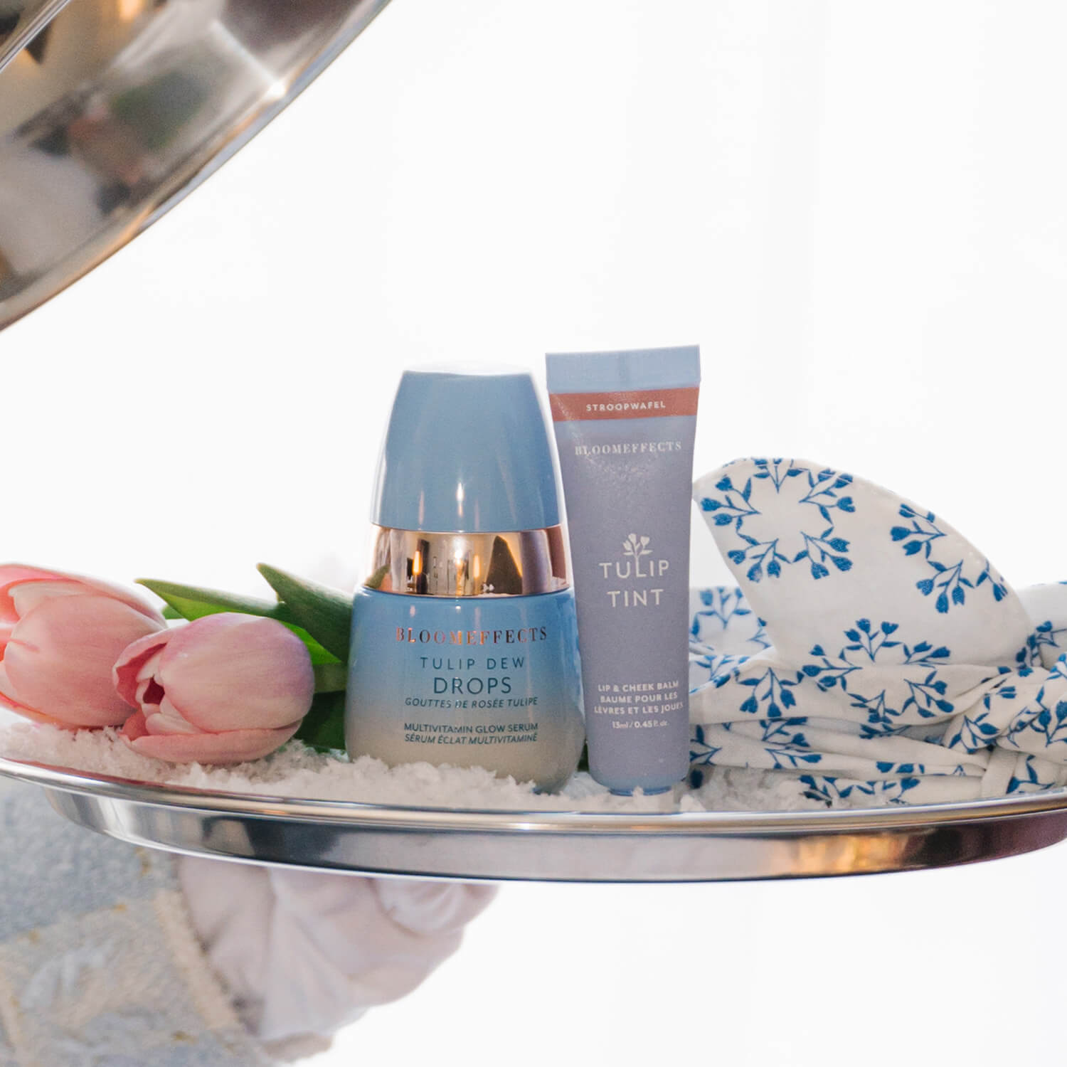 Two skincare products on a tray with tulips and a floral towel.