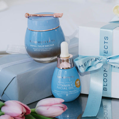 Blue skincare product with a dropper bottle and pink tulips on a reflective surface.