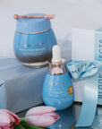 Blue skincare product with a dropper bottle and pink tulips on a reflective surface.