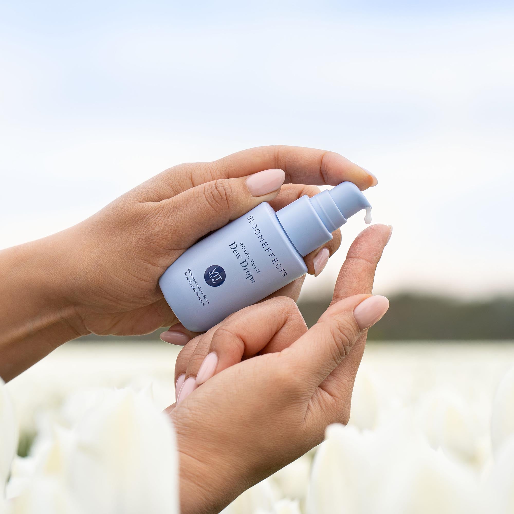 Hand holding a Tulip Dew Drops bottle with a blurred floral background