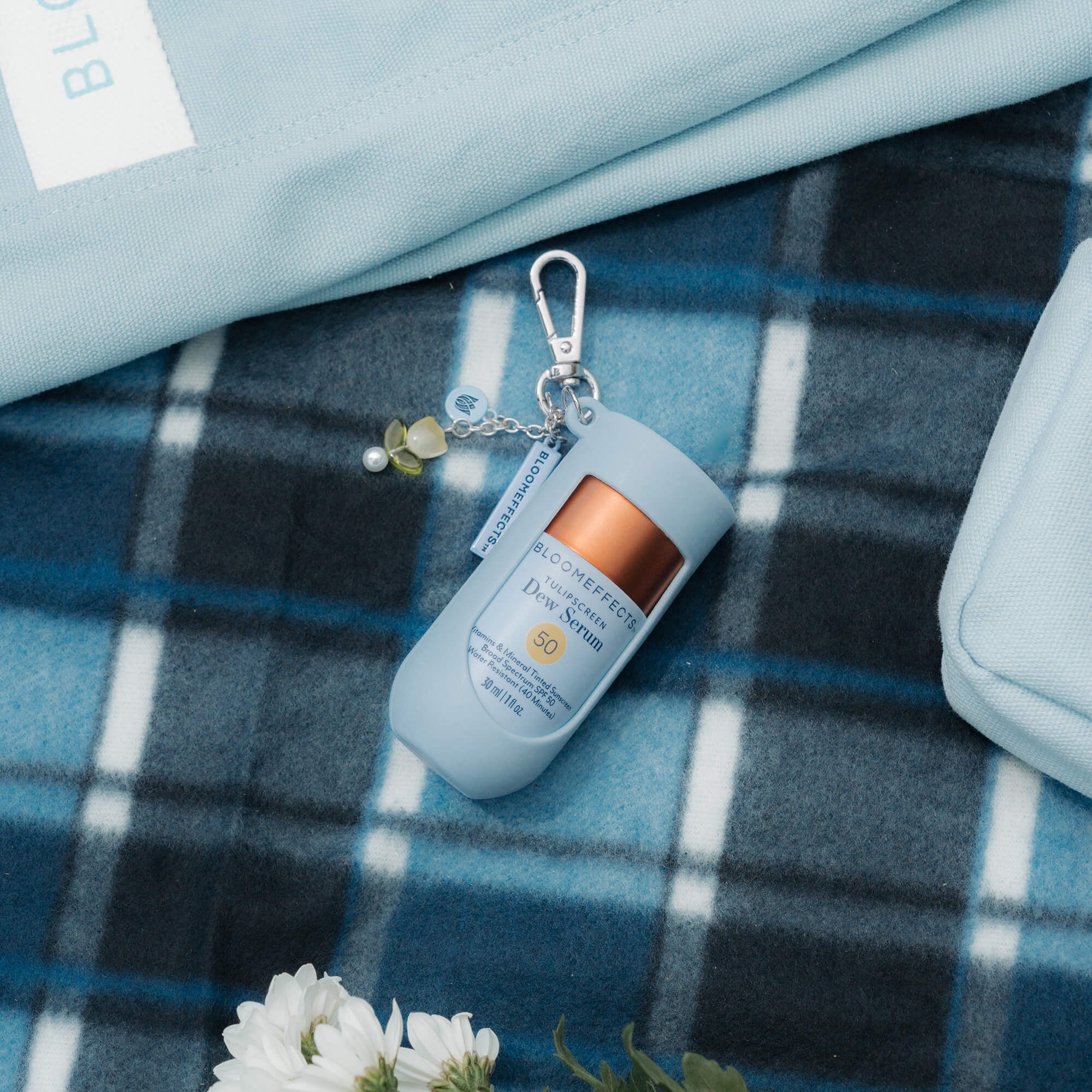 Keychain with Bloomeffects skincare product on a blue plaid fabric background
