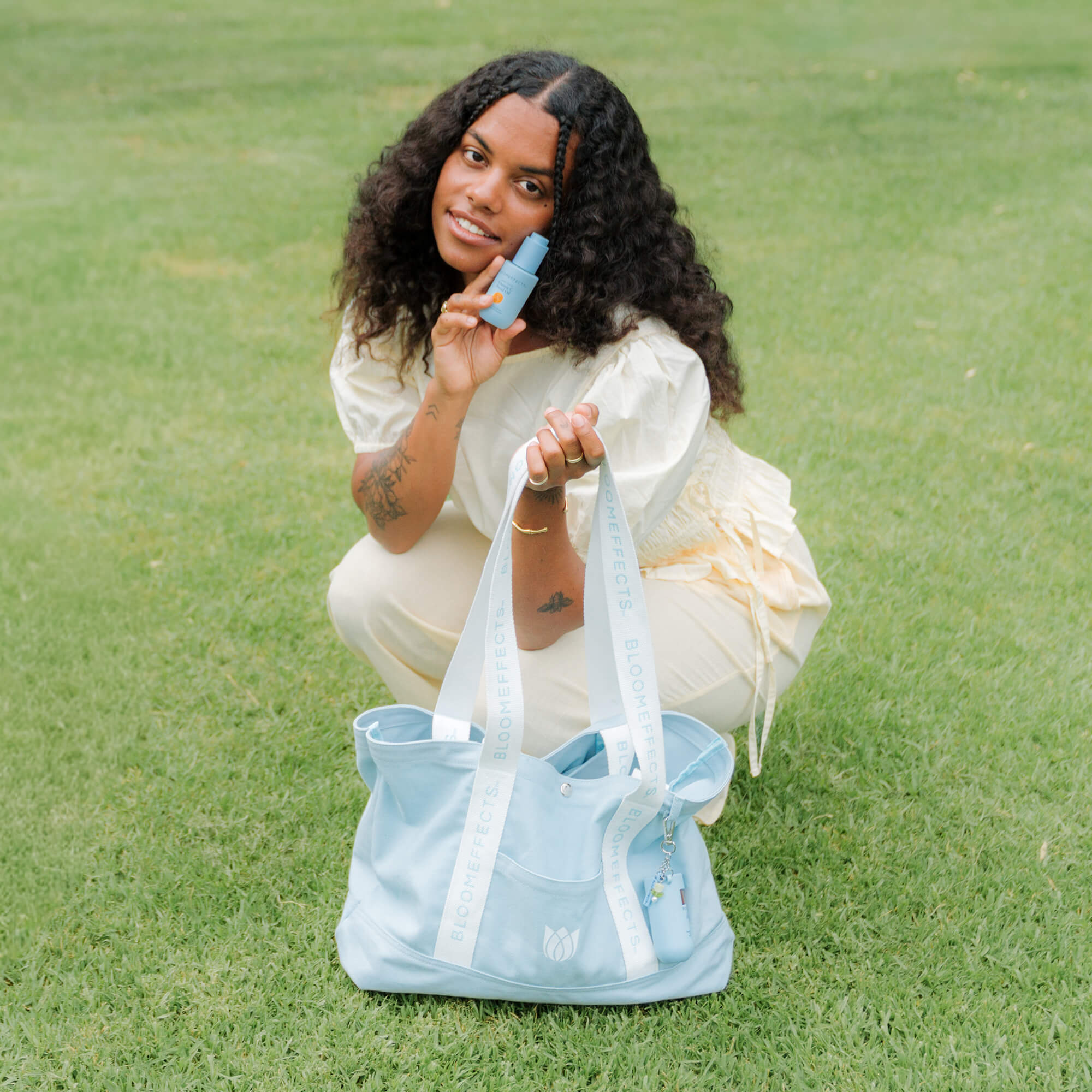 Woman holding a light blue Bloomeffects tote bag on grass