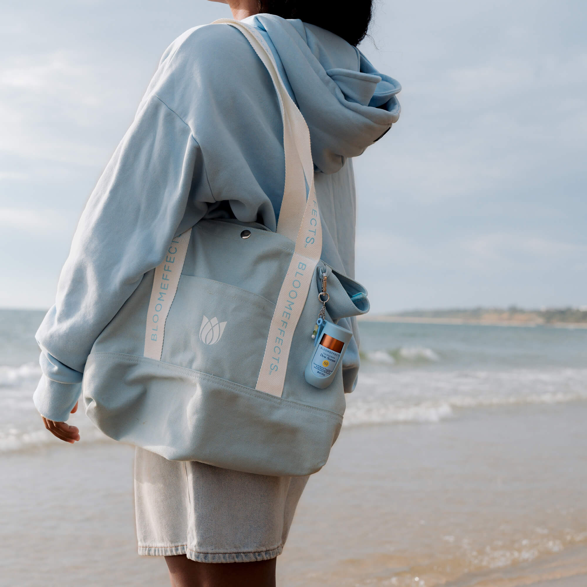 Person wearing a light blue hoodie and shorts with a matching bag on a beach.