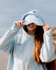 Person wearing a light gray hoodie with a logo on a beach