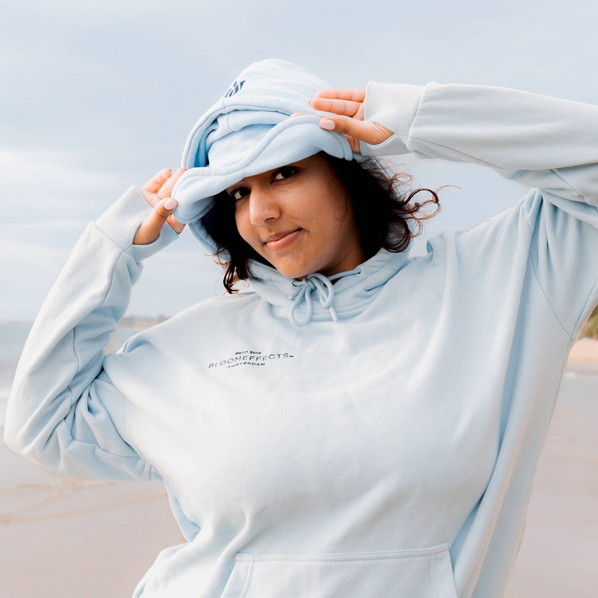 Person wearing a light blue hoodie with a brand logo, standing against a light background