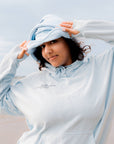 Person wearing a light blue hoodie with a brand logo, standing against a light background
