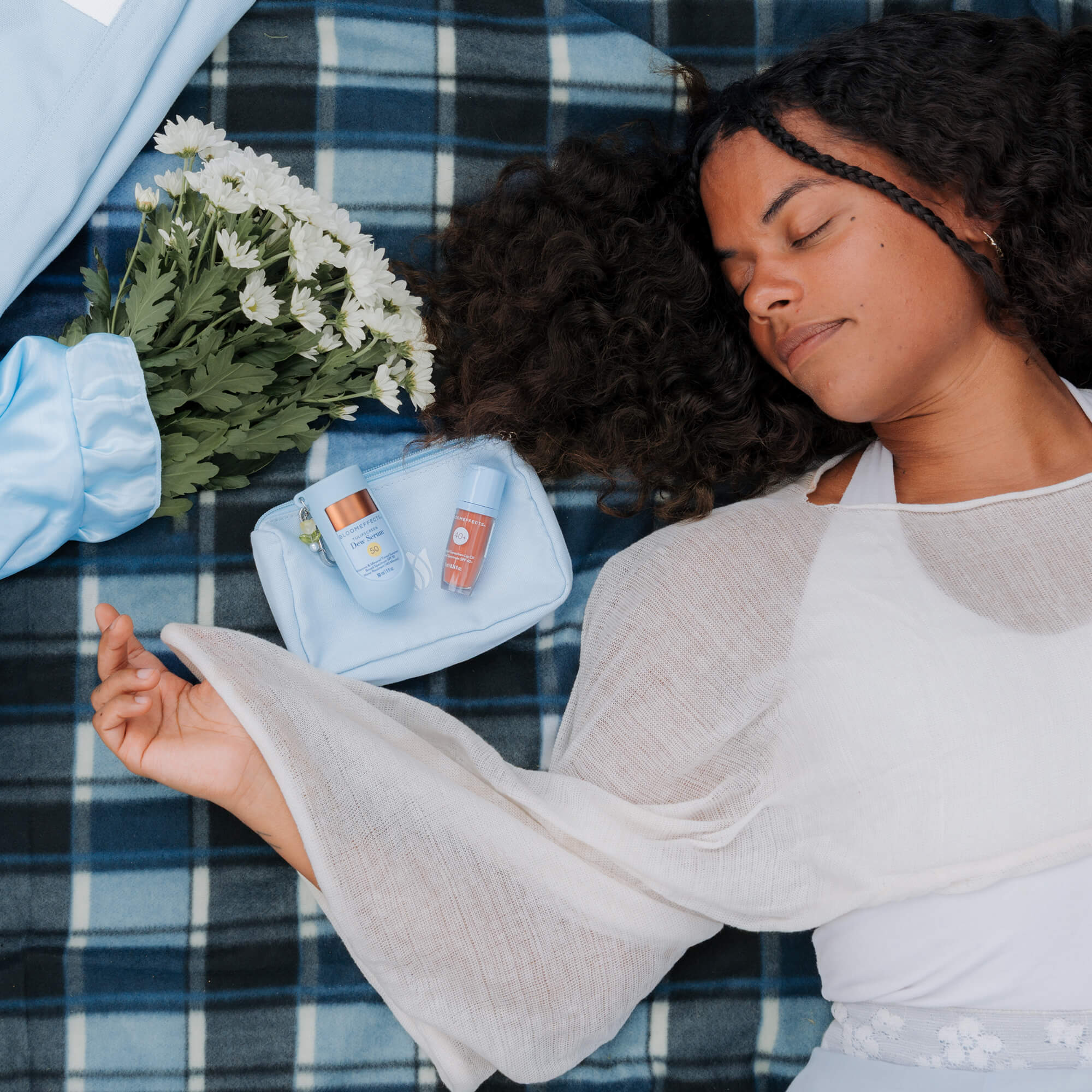 Woman lying on a plaid blanket, surrounded by Bloomeffects products and flowers.