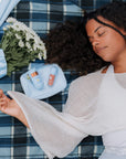 Woman lying on a plaid blanket, surrounded by Bloomeffects products and flowers.