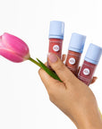 Hand holding three lip oils with a pink tulip against a white background