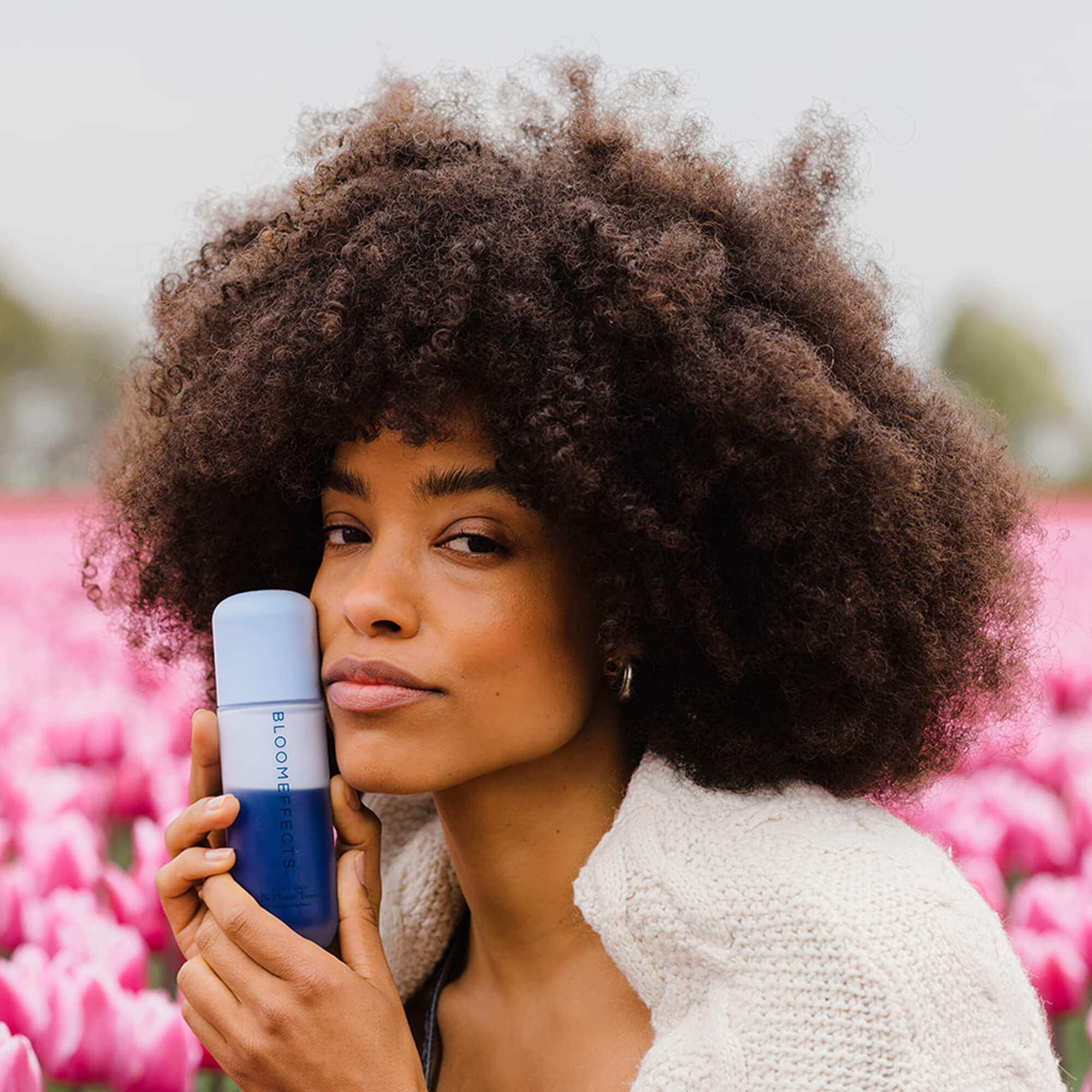 Woman holding a Bloomeffects Tonic bottle with pink flowers in the background

